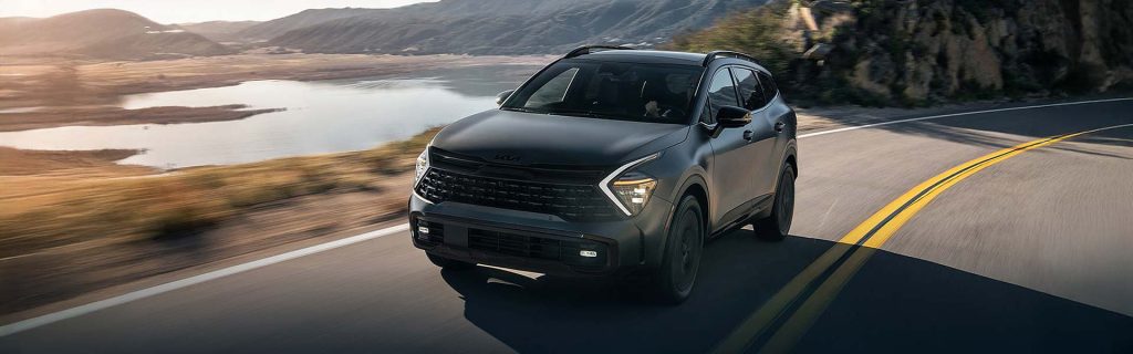 A Kia Sportage Hybrid driving along a scenic mountain road with a lake visible in the background.