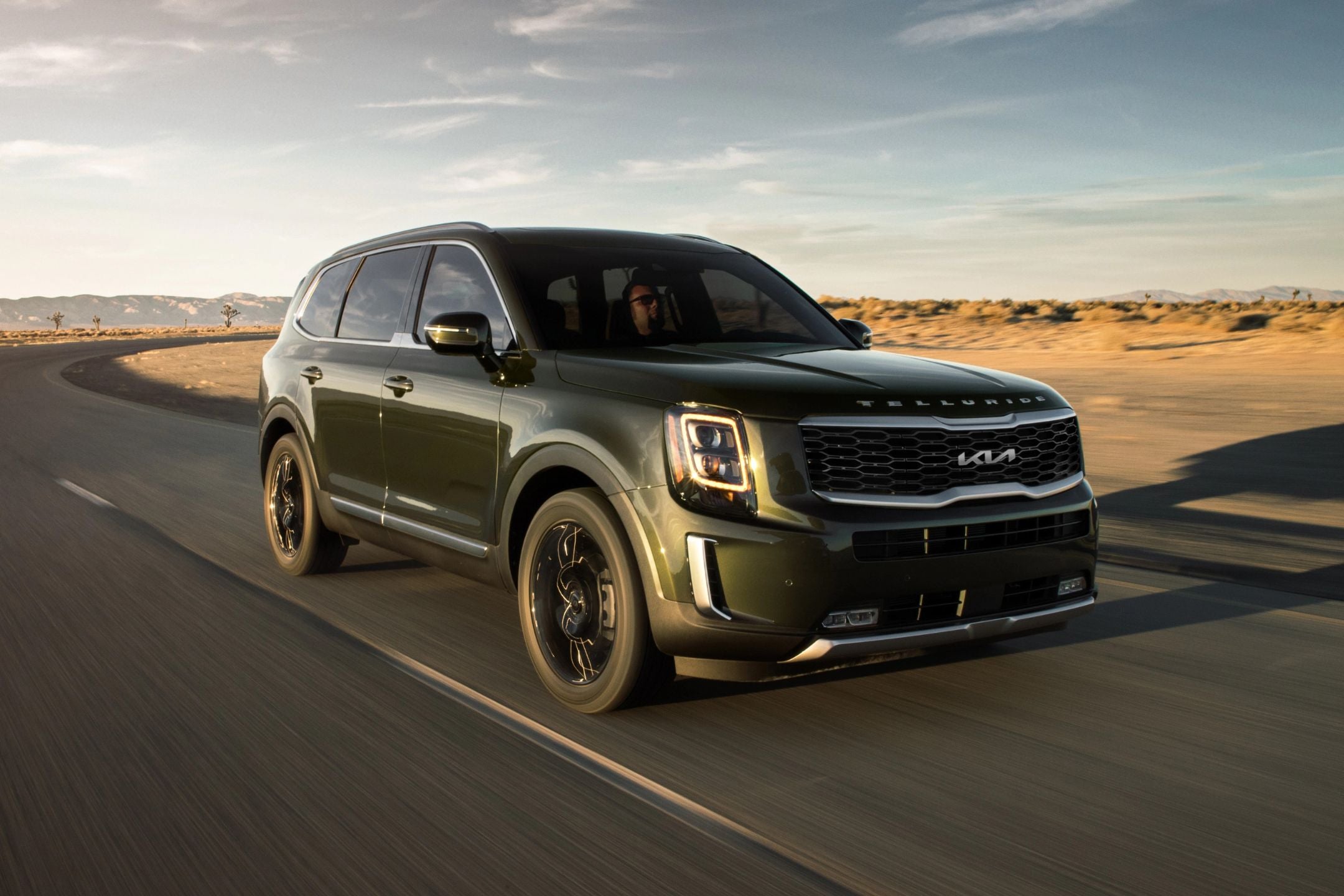 Green Kia SUV driving on a desert road with a scenic landscape background